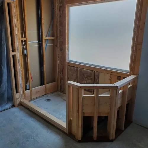 Partially finished bathroom in Bullhead City with open wall studs, plumbing, plank flooring, and framed shower by frosted window.
