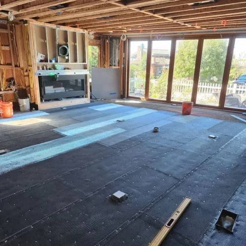 Interior of a Bullhead City home under remodel with exposed beams, large windows, and flooring materials on the floor.