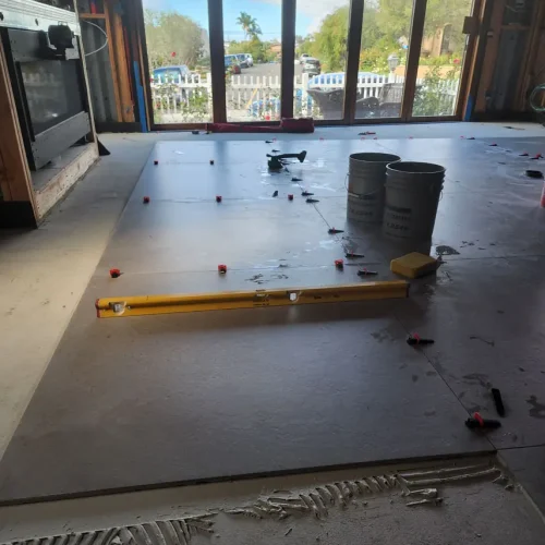 Large floor tiles are being installed for a kitchen remodel in Bullhead City, with tools and sliding doors to the outdoors.