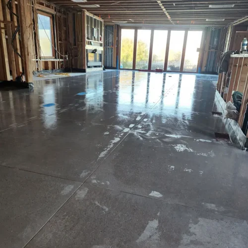 An unfinished room in Fort Mohave shows exposed framing, polished concrete, big windows, and visible flooring materials.